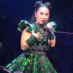 a woman in a green and black dress holding a microphone while standing on a stage