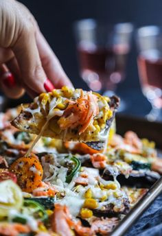 a person scooping some food out of a pan with other foods on it and wine glasses in the background