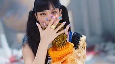 a woman with black hair and colorful nails holds her hand up to her face