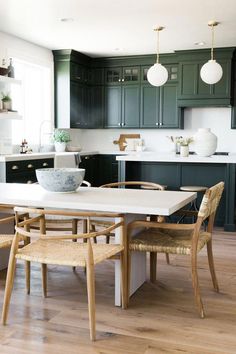 a kitchen with dark green cabinets and white counter tops is pictured in this image, there are wooden chairs around the table