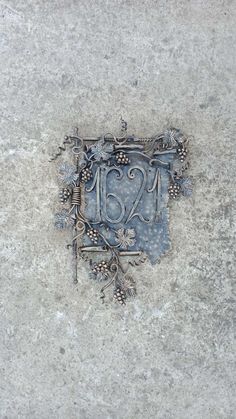 a decorative metal plaque on the side of a cement wall with vines and leaves around it