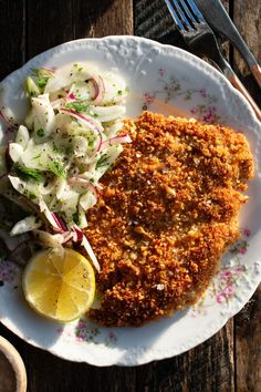 a white plate topped with fish and coleslaw next to a lemon wedge on top of a wooden table