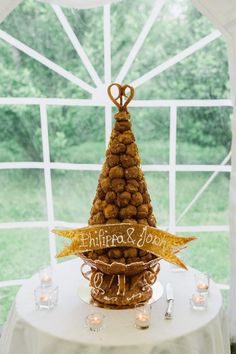 a table topped with a cake covered in donuts next to a large window filled with white curtains