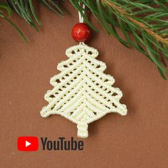 a crocheted christmas tree ornament hanging from a pine tree branch with the youtube logo below