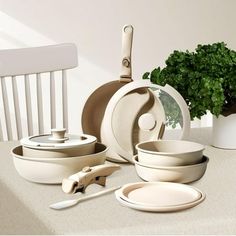 a table topped with lots of white dishes next to a potted leafy plant