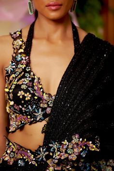 Black is your new summer romantics to go all glam for any intimate soiree of the season. This pre-draped saree highlighted with the lines of black bead-work all around comes with a dazzling floral blouse accentuated with embroidered multicolor bead-work and cut-work. The floral bead embroidery also highlights the waistline and goes on the pallu’s borders. Sleeveless blouse with a deep neck and cutwork detailing at the edges. Hook at the back of the blouse. The silk satin pre-draped saree is acce Saree Edging Ideas, Elegant Evening Pre-draped Saree With Resham Embroidery, Elegant Black Embellished Pre-draped Saree, Glamorous Black Fitted Pre-draped Saree, Elegant Black Pre-draped Saree With Mirror Work, Glamorous Festive Embellished Pre-draped Saree, Evening Georgette Pre-draped Saree With Mirror Work, Glamorous Hand Embellished Pre-draped Saree For Party, Elegant Party Pre-draped Saree With Zari Work