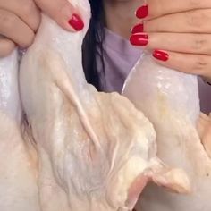 a woman holding up two pieces of chicken in front of her face with red nail polish