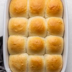 a baking dish filled with bread rolls on top of a white countertop next to a black towel