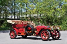 an old red car is parked on the side of the road in front of some trees