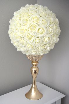 a gold vase filled with white roses on top of a table next to a wall