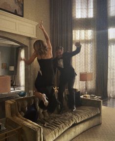 two people jumping on top of a couch in a living room next to a window