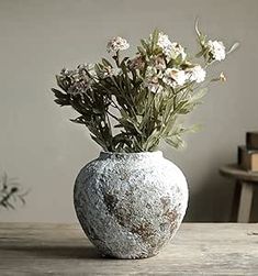 a white vase with flowers in it sitting on a table next to a bookcase