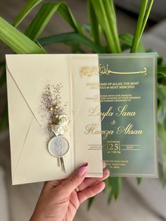 a person holding up a wedding card with a flower on the front and an envelope in the back