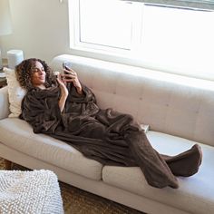 a woman laying on top of a white couch under a blanket while holding a cell phone