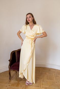 a woman wearing a yellow dress standing in front of a chair with her hands on her hips