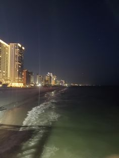 the city lights shine brightly in the night sky over the ocean and beach as seen from an airplane