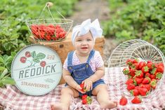 a baby sitting on a blanket with strawberries in front of her and two baskets full of strawberries