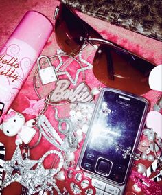 a cell phone, sunglasses, and other items are on a pink blanket with glitter