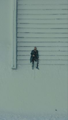 a man sitting in the snow next to a garage door