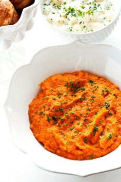 two bowls filled with mashed potatoes next to other dishes on a white tablecloth