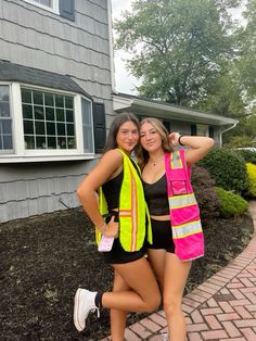 two young women in safety vests posing for a photo on a brick walkway next to a house