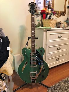 a green guitar sitting on top of a hard wood floor next to a white dresser