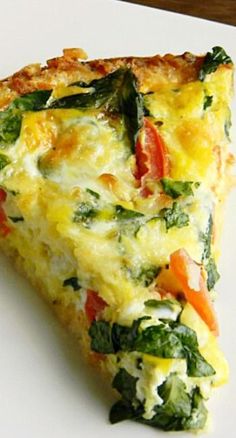 a slice of quiche on a white plate with spinach and tomato toppings