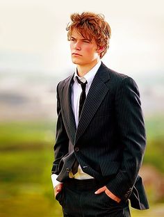 a young man wearing a suit and tie standing in front of a scenic view with his hands on his hips