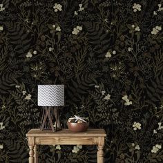 a wooden table with a lamp on it next to a wallpapered plant pattern