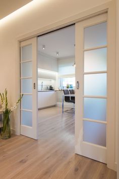 an open door leading to a living room and dining room with white walls, hardwood flooring and glass sliding doors