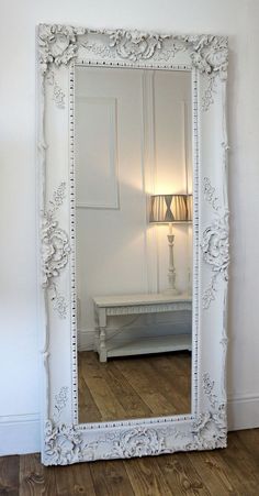 a large white mirror sitting on top of a wooden floor next to a light fixture