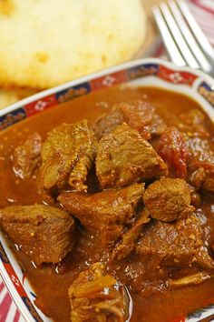 a red and white bowl filled with meat curry