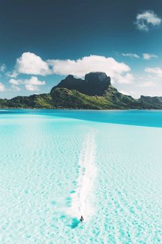 the water is crystal blue and there are clouds in the sky above it, with an island in the distance