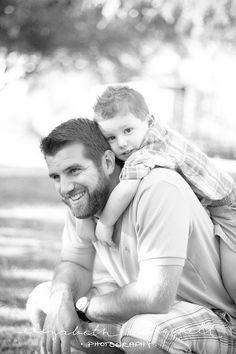 a man holding a little boy in his arms while sitting on the ground under a tree