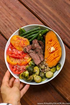 a person holding a bowl full of vegetables and meat on a wooden table with text overlay