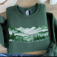 This misty mountain forest design is printed directly on a classic Gildan unisex sweatshirt with drop sleeves. When you think of a sweatshirt, this is one that should come to mind. If you prefer an oversized look, go up 1-2 sizes.  As all of our shirts are made to order, there are no refunds - make sure you are ordering the correct size. If there is any problem whatsoever with the printing or the garment itself, please contact me for assistance.  * 50% cotton, 50% polyester * Pre-shrunk * Classi Green Crew Neck Top For Adventure, Green Long Sleeve Sweatshirt For Outdoor Activities, Winter Hiking Crew Neck Top, Green Crew Neck Sweatshirt For Outdoor, Outdoor Long Sleeve Cotton Tops, Green Cotton Sweatshirt With Custom Print, Green Cotton Outdoor Sweatshirt, Green Cotton Sweatshirt For Outdoor, Long Sleeve Cotton T-shirt For Hiking