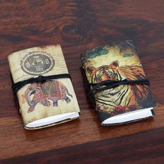 two small notebooks are sitting on a wooden table, one has an elephant and the other is a tiger