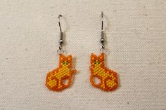 Glass seed beads of bright orange and yellow, hand woven to form a green eyed orange tabby cat.  Very light weight and cute jewelry for any occasion.  Stainless steel ear wire. Cat Earrings Diy, Seed Bead Cat, Beading Earring, Studded Pumpkin, Beaded Cat, Cat Orange, Orange Tabby Cats, Pumpkin Earrings