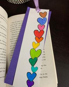 an open book with paper hearts on it and a purple ribbon hanging from the book