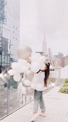 a woman is holding white balloons in front of a cityscape with skyscrapers