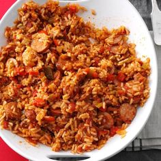 a white bowl filled with rice and sausage on top of a red table cloth next to a fork