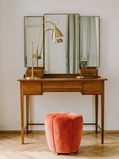 an orange ottoman sits in front of a desk with a mirror and lamp on it