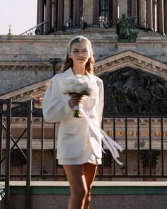 a woman holding a bouquet of flowers in front of a building with statues on it