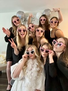 a group of women wearing pink heart shaped sunglasses pose for a photo in front of a mirror