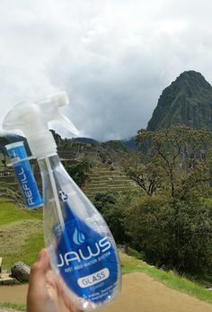 a hand holding a bottle of water in front of a mountain range with rice terraces