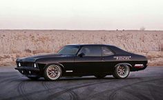 a black muscle car parked in a parking lot next to a dry grass covered field