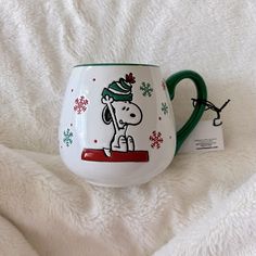 a white and green coffee mug with a cartoon dog on it's side next to a tag