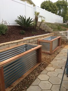 two wooden planters sitting next to each other on a stone walkway in front of a white fence