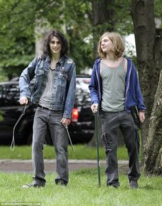 two young men standing next to each other on top of a lush green field with trees