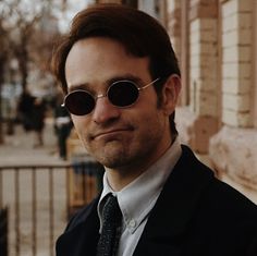 a man wearing sunglasses and a suit standing in front of a building